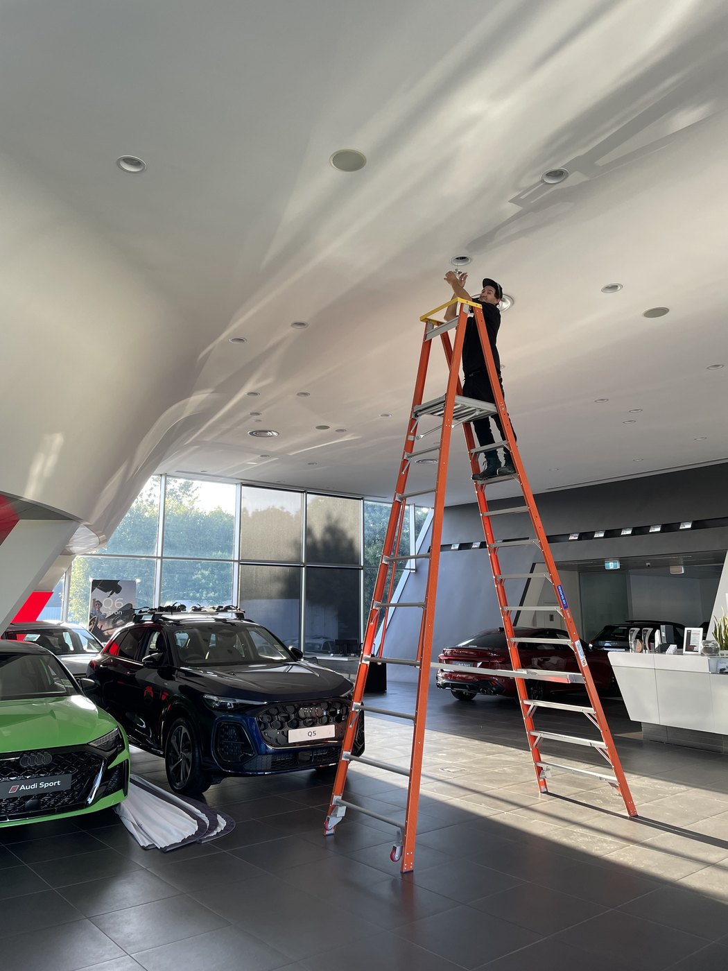 SALTD Electrical electrician on a ladder replacing downlights in a car dealership showroom