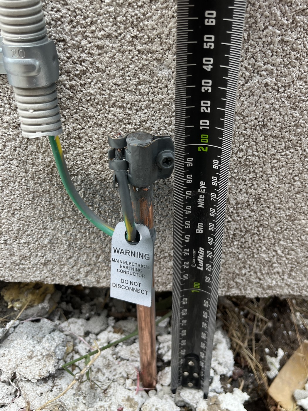 New copper main earth electrode driven into the ground beside a house wall, with the earthing conductor clamped to it and a do-not-disconnect warning tag fitted, installed by SALTD Electrical
